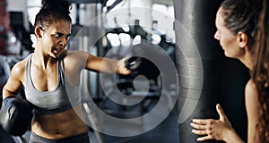 Watch your form. Cropped shot of a young female boxer working out on a punching bag with her trainer in the gym.