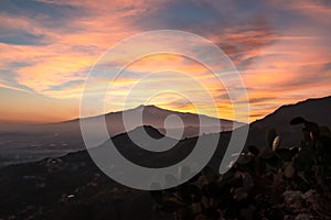 Watching beautiful sunset behind volcano Mount Etna near Castelmola, Taormina, Sicily. Clouds with vibrant red orange colors