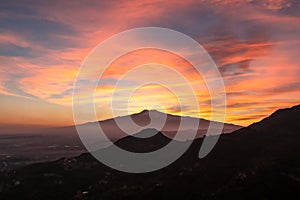 Watching beautiful sunset behind volcano Mount Etna near Castelmola, Taormina, Sicily. Clouds with vibrant red orange colors