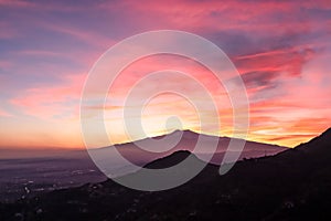 Watching beautiful sunset behind volcano Mount Etna near Castelmola, Taormina, Sicily. Clouds with vibrant red orange colors