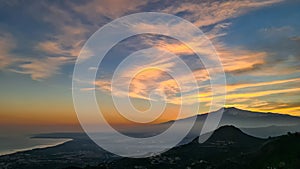 Watching beautiful sunset behind volcano Mount Etna near Castelmola, Taormina, Sicily. Clouds with vibrant red orange colors