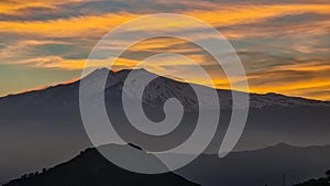 Watching beautiful sunset behind volcano Mount Etna near Castelmola, Taormina, Sicily. Clouds with vibrant red orange colors