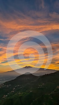 Watching beautiful sunset behind volcano Mount Etna near Castelmola, Taormina, Sicily. Clouds with vibrant red orange colors