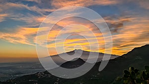 Watching beautiful sunset behind volcano Mount Etna near Castelmola, Taormina, Sicily. Clouds with vibrant red orange colors