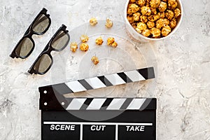 Watching film. Clapperboard, glasses and popcorn on grey stone background top view copyspace