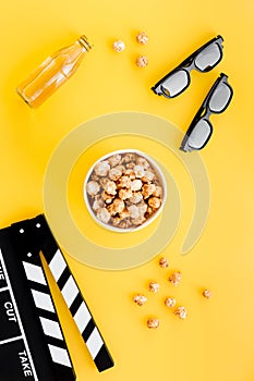 Watching film. Clapperboard, glasses and popcorn on yellow background top view