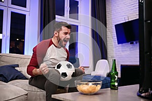 Watching a game. Cheerful young men drinking beer and eating snacks while watching TV