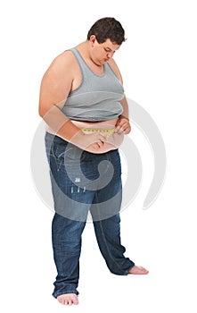 Watching his weight. An obese young man measuring his waist with a measuring tape against a white background.