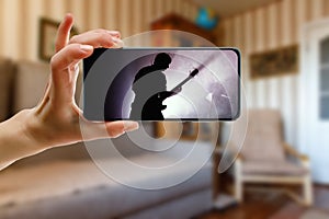 Watching online music concert at home using a mobile phone. Guitarist silhouette on the screen