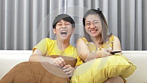 Watching TV lying on the couch. asian Mom and son watch TV together and smile. Mom switches channels. slow motion