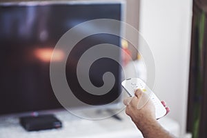 Watching TV. A man`s hand holding the TV remote control with a television in the background