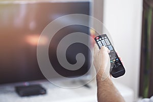 Watching TV. A man`s hand holding the TV remote control with a television in the background