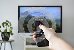 Watching TV. A woman`s hand holding the TV remote control with a television in the background