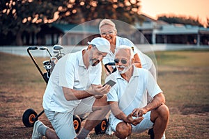 Watching the video. Senior golfers on court. Two men using smart phone