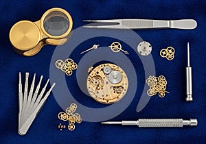 Watchmaking tools and components are arranged on a deep blue