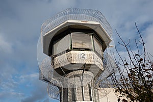 Watchtower of a correctional facility of a prison with a balustrade and two rows of barbed wire rolls in front of a dramatic sky