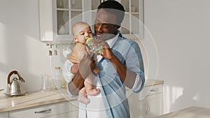 Water balance. African american father carrying newborn baby, coming to kitchen and giving baby bottle to thirsty kid