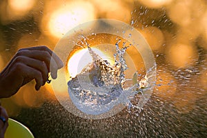 A water balloon bursting with a sunset sky in background, conceptual image.