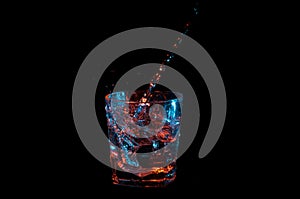 Clear liquid being poured into a spiral in a rocks glass under blue and orange lights isolated on a black background