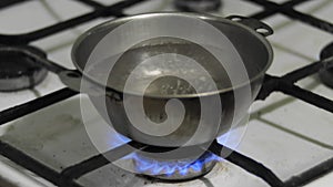 Water is boiling in a metal pot. Bowl of water warmed on a dirty old gas stove at home, close up. Poverty destitution