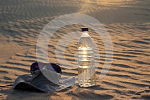 Water bottle, hat and sunglasses lying on the sand in the desert