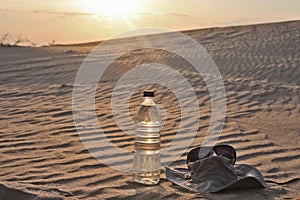 Water bottle, hat and sunglasses lying on the sand in the desert