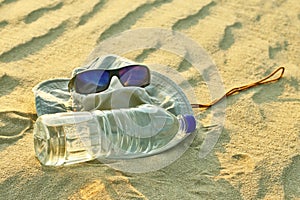 Water bottle, hat and sunglasses lying on the sand in the desert