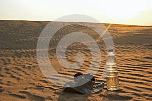 Water bottle, hat and sunglasses lying on the sand in the desert