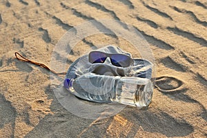 Water bottle, hat and sunglasses lying on the sand in the desert