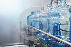 Water bottling conveyor line with plastic bottles or gallons on water factory production, selective focus for copy space