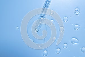 Water bubbles with cosmetic liquid drops of serum on a blue background of a laboratory glass pipette. Close-up of a