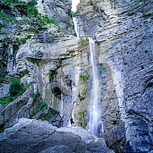 Water cascade on rock wall falling from great height with person standing on rock looking at the water