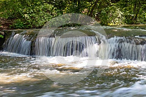 Water cascading over rocks in a woodland stream, sunlight and shade with heavy foliage