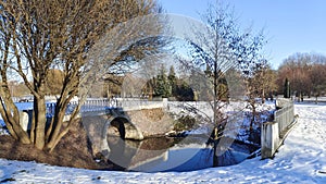 The water channel in the park flows under the bridge and is partially covered with ice in winter. Willows, alders and spruces grow