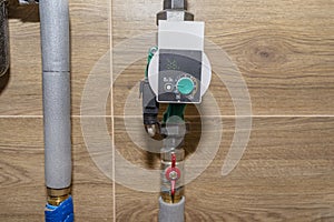 Water circulation pump for underfloor heating in a modern gas boiler room lined with ceramic tiles.