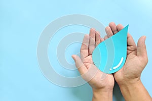 Water conservation and access to safe drinking water concept. Top view of human hands holding blue water drop with copy space.