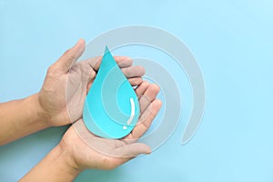 Water conservation and access to safe drinking water concept. Top view of human hands holding blue water drop with copy space.