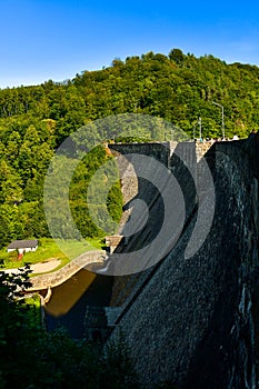 Water dam on the Bystrzyca river, green forest on the hillside, view from the dam on a sunny summer day