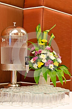 Water dispenser with glasses and flower vase at reception
