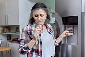 Water dispenser, woman taking cold water into glass from home refrigerator