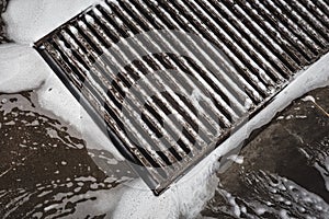 Water drainage grill on the car wash, foam flowing into the sink