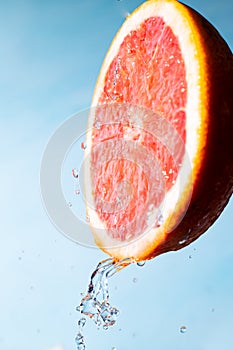 Water drips from half a grapefruit. Splashes and drops fly from a piece of grapefruit symbolizing the brightness and freshness of