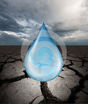 Close up view of water drop against ground cracked with heat and stormy sky