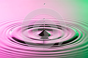 Water drop close with concentric ripples on colourful pink and green surface