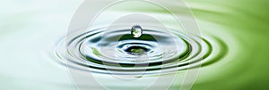 Water drop creating ripples on green liquid surface