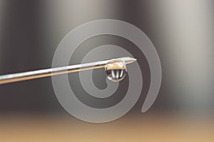 Water drop falling from the syringe needle against grey background