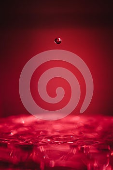 Water drop midair above bowl of water red background