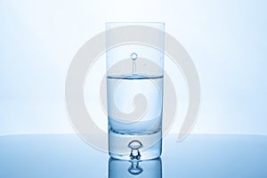 Water drop splash inside glass half full against bright background