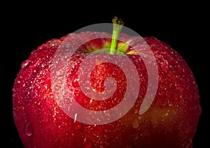 Water droplet on glossy surface of red apple on black background