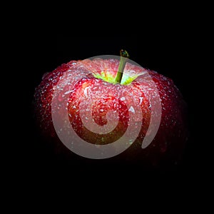 Water droplet on glossy surface of red apple on black background